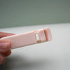 A hand holds a pink cartoon mini eyelash curler against a light green background.