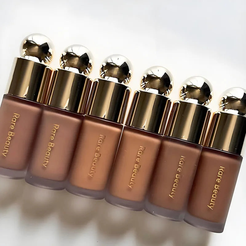 A row of liquid bronzer contour foundation sticks with gold caps lined up on a white surface.
