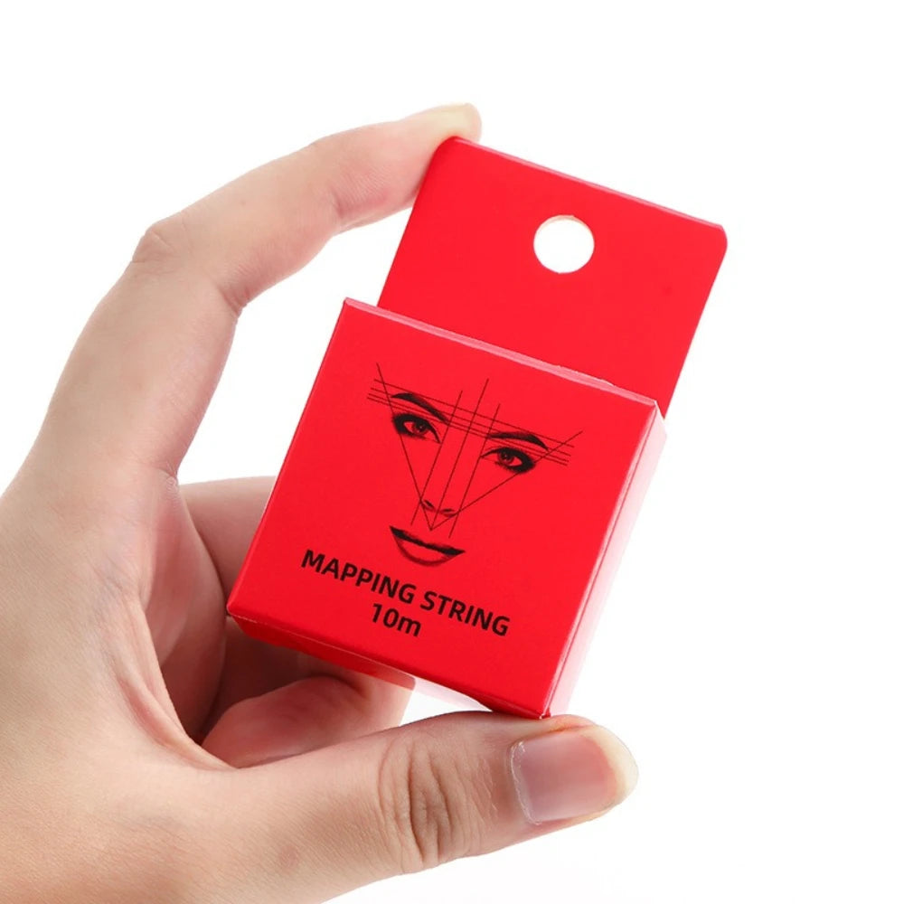 A hand holds a red pre-inked eyebrow mapping string package with a hole for threading.