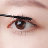 A close-up of an eye with false eyelashes being curled by a black eyelash curler.