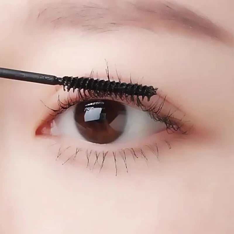 A close-up of an eye with false eyelashes being curled by a black eyelash curler.