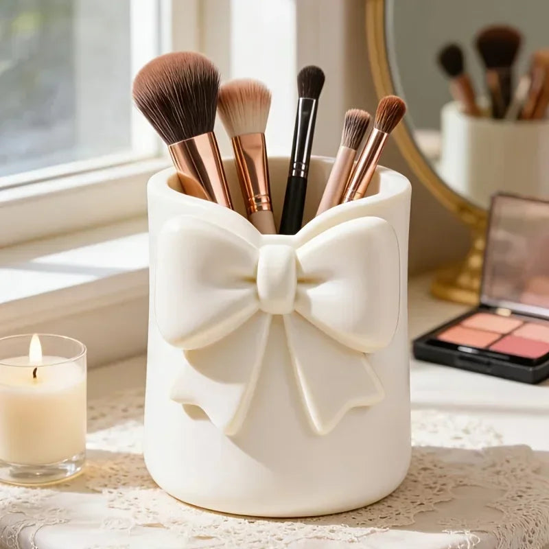 Organisateur de rangement en céramique blanche avec un nœud qui contient plusieurs pinceaux de maquillage et une bougie sur u