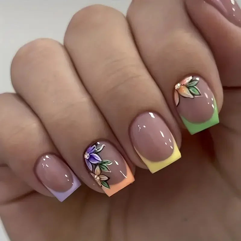 A close-up of a hand displaying press-on acrylic flower nails with soft pink and green accents.