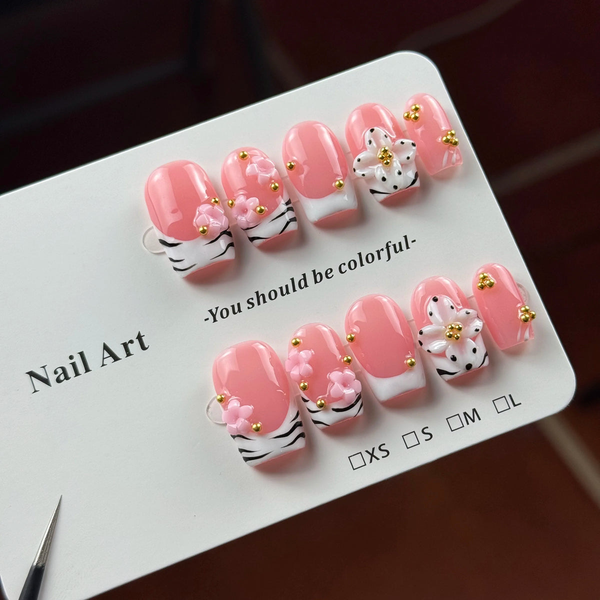 A set of hand-painted pink resin nail art designs featuring white accents and gold floral details.
