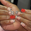 A hand displays a set of nude pink press-on nails decorated with leopard print and 3D silver charms.