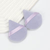 A pair of lavender cosmetic powder puffs with a light purple ribbon detail resting on a white surface.