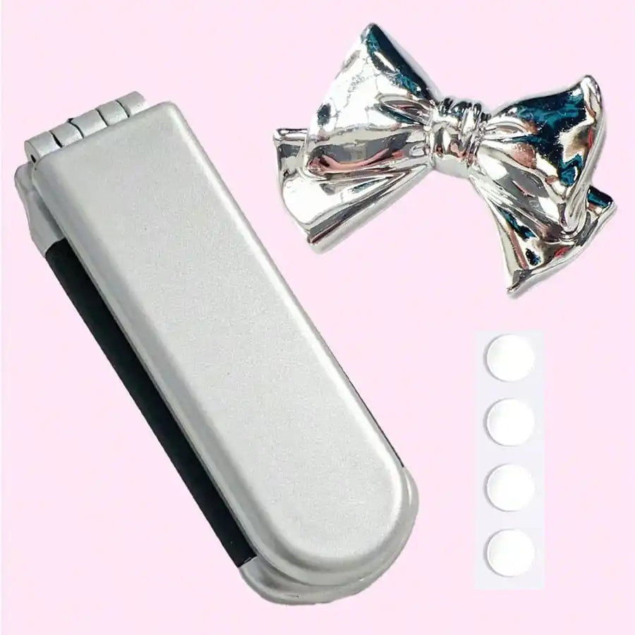 A silver portable compact comb with an airbag and mirror next to a shiny silver bow.