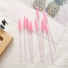 A collection of pink and clear disposable eyelash and eyebrow makeup brushes are displayed on a white surface next to a pinea