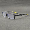 Un par de gafas deportivas para leer grises oscuras anti-luz azul con detalles amarillos, apoyadas sobre una superficie gris 
