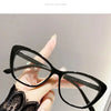A hand is holding a pair of black cat eye reading glasses against a light gray background.