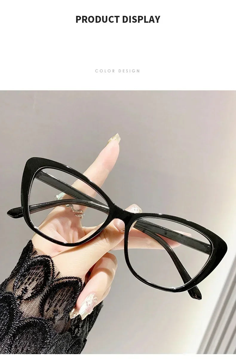 A hand is holding a pair of black cat eye reading glasses against a light gray background.
