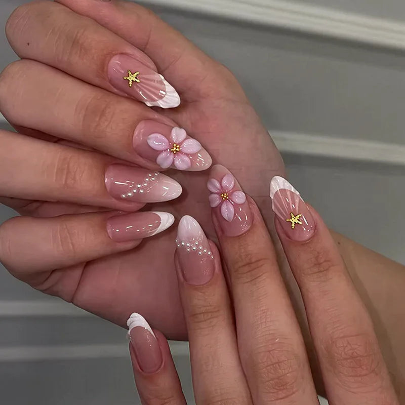 A close-up of a hand displaying 24-piece almond press-on nails featuring floral and butterfly designs.