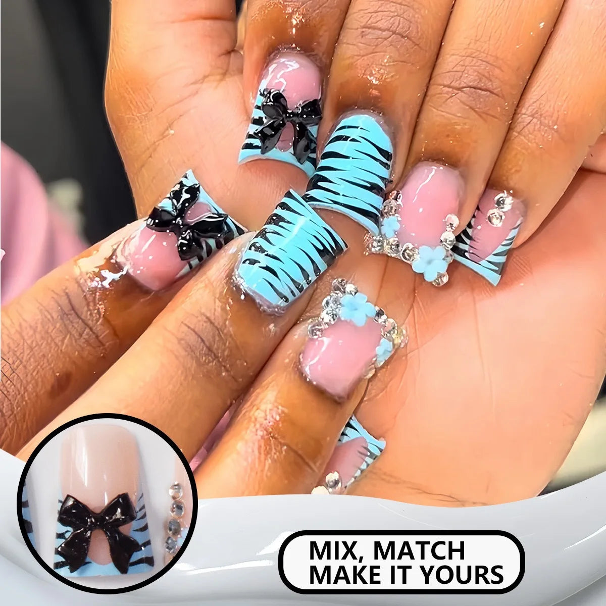 Close-up of hands displaying nude pink press-on nails with black bow and blue zebra stripes and silver charms