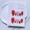 A set of red and pink Y2K almond press-on nails with floral designs displayed on a white card.