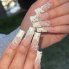 A close-up of a hand displaying various reusable nail extension forms with silver and iridescent glitter stars.