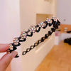 A hand holds a black rhinestone wave headband decorated with floral embellishments.