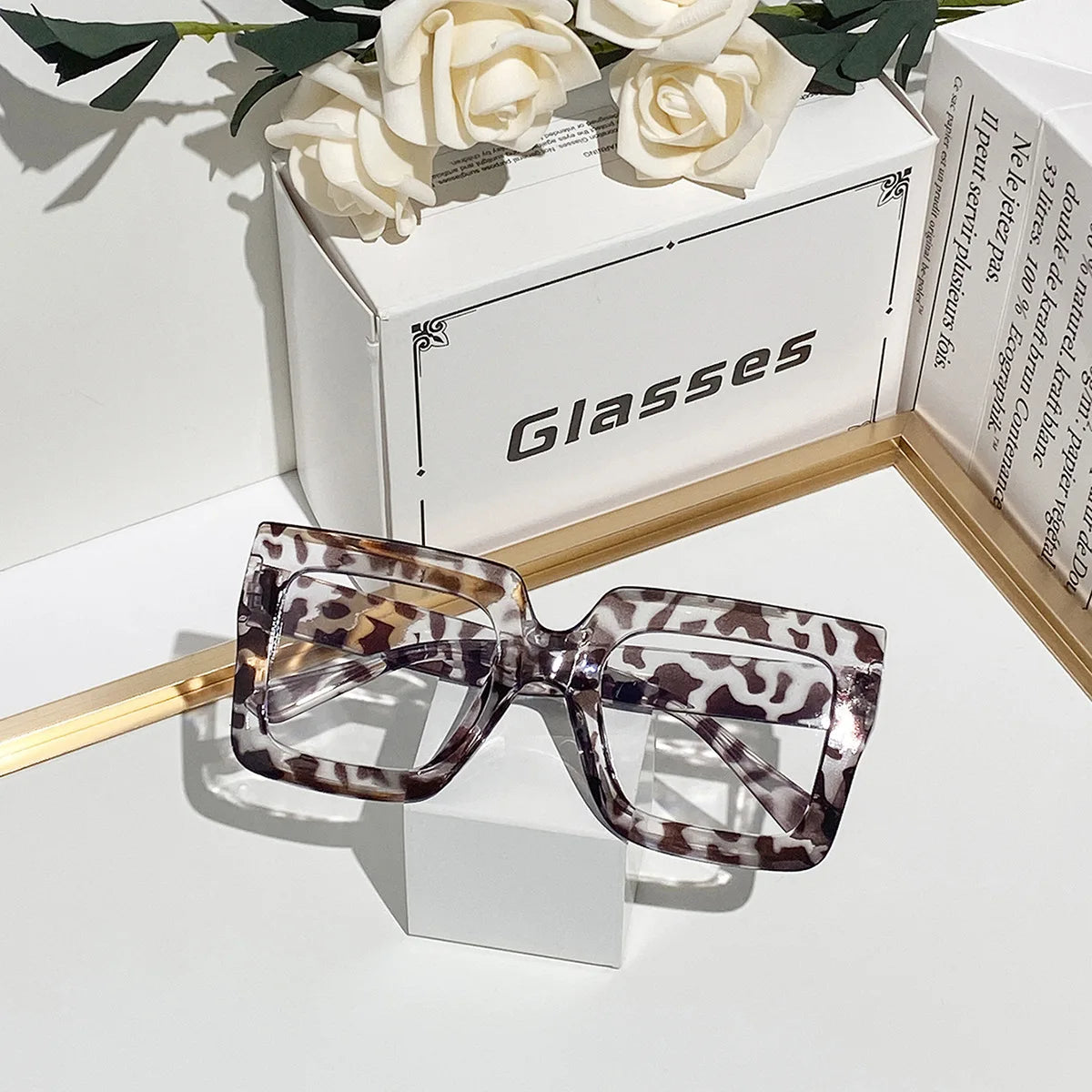 A pair of tortoiseshell patterned square eyeglasses with clear lenses displayed on a white box.