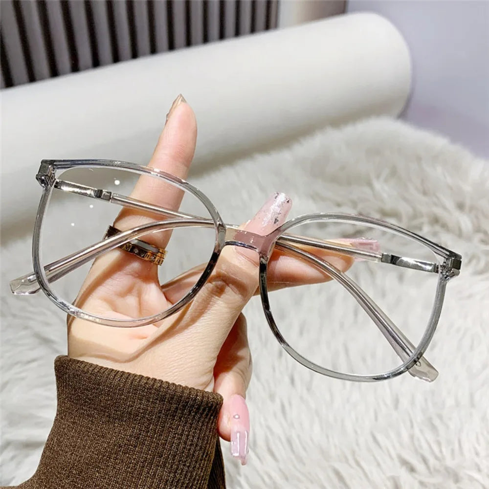 Une main tient une paire de lunettes à monture fine et claire, de style œil de chat, sur un fond blanc duveteux.