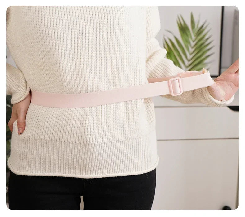 Eine Person trägt einen beigen Pullover und hält ein pinkes beheiztes Bauchmassierband.