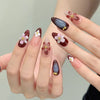 Une main montre un ensemble de faux ongles press-on roses à l'amande française avec des accents floraux sur les bouts des doi