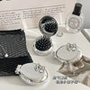 A set of silver folding massage combs and a makeup mirror displayed on a white surface.