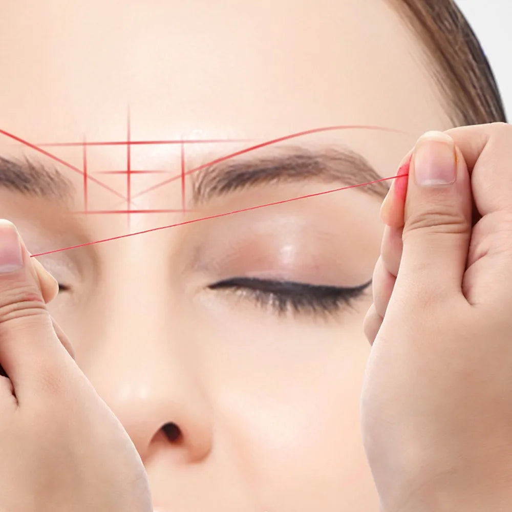 Hands are mapping an eyebrow line on a woman's face using a red thread for microblading guidance.