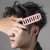 A hand is holding a pink volumizing wide-tooth hair styling comb against a person's dark hair.
