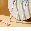 Three silicone tongue scrapers in purple, teal, and white are displayed against a neutral background.