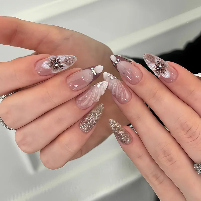 Une main montre un ensemble d'ongles press-on roses à l'amande française avec des accents floraux sur les bouts des doigts.