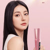 A woman with long black hair holds a pink hair straightener and curler against a light pink background.