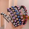 A hand holds a black rhinestone wave headband featuring colorful floral embellishments.
