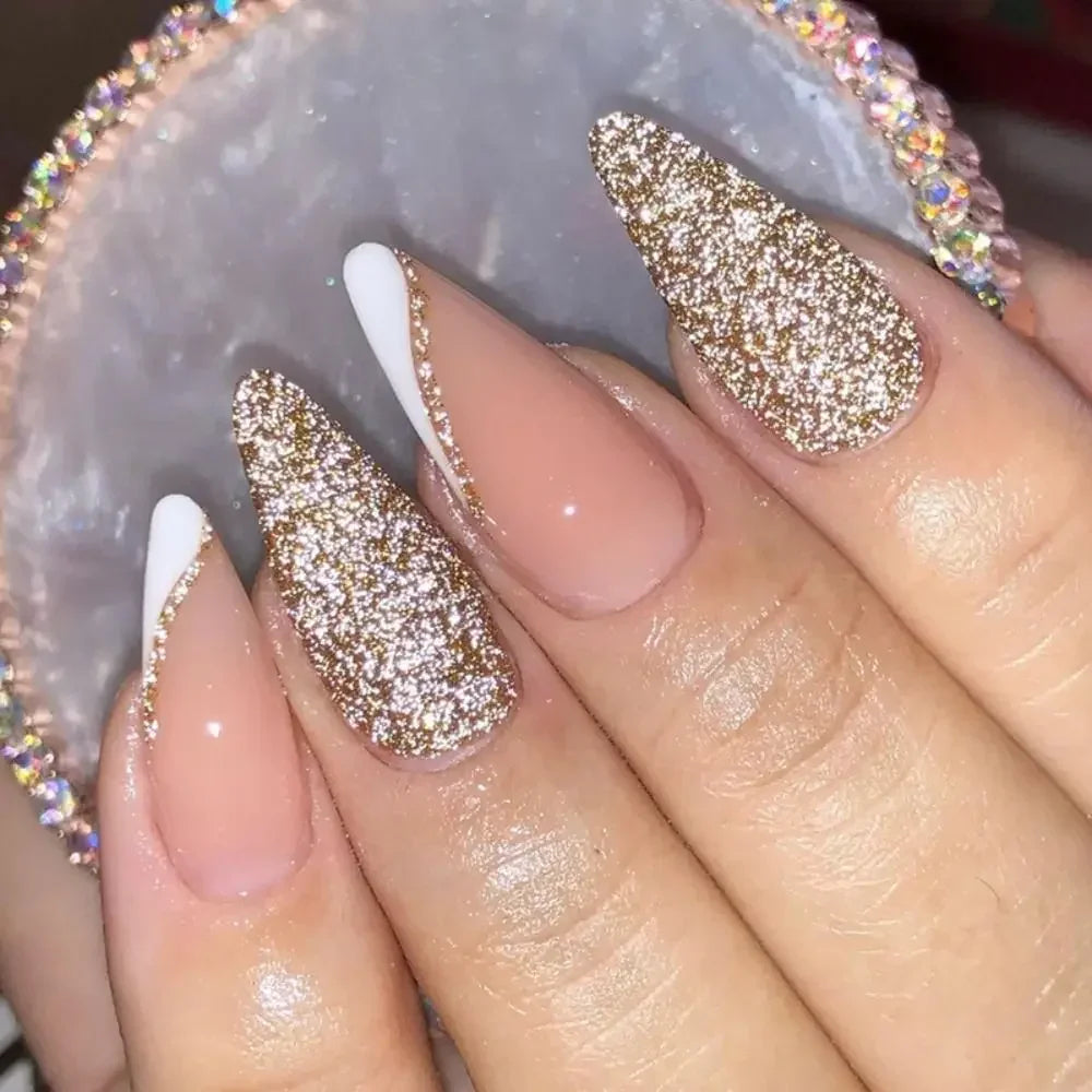 A close-up of a hand displaying press-on false nails with a gold glitter finish and white accents on a light background.