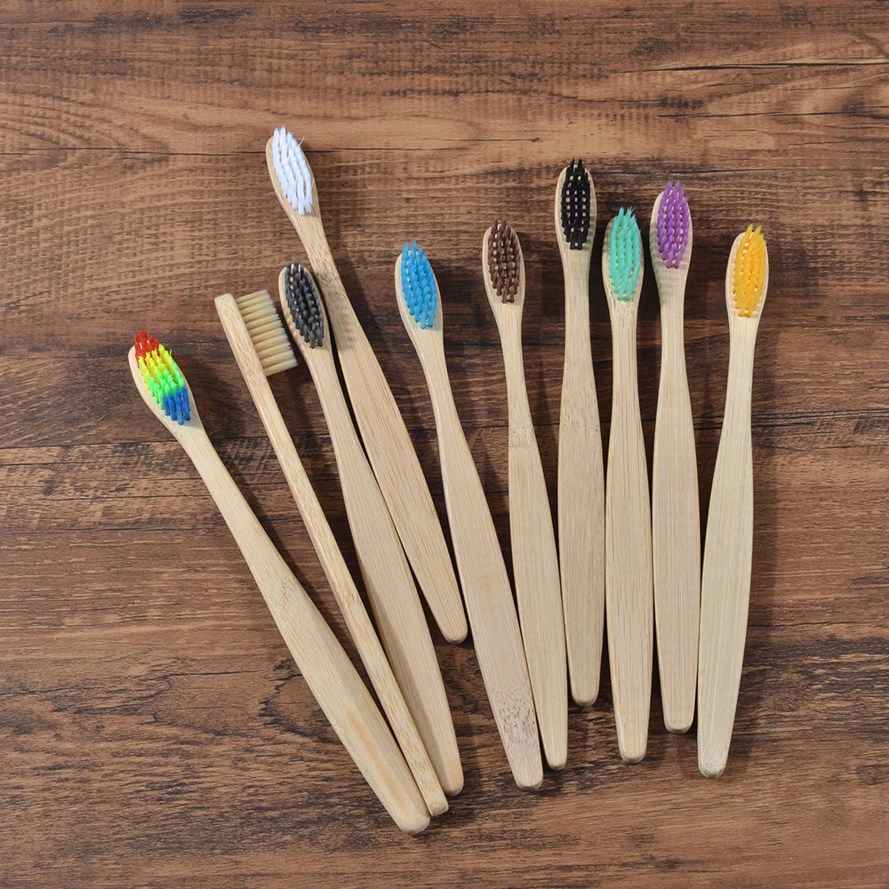 A collection of ten natural bamboo toothbrushes in various colors laid out on a wooden surface.