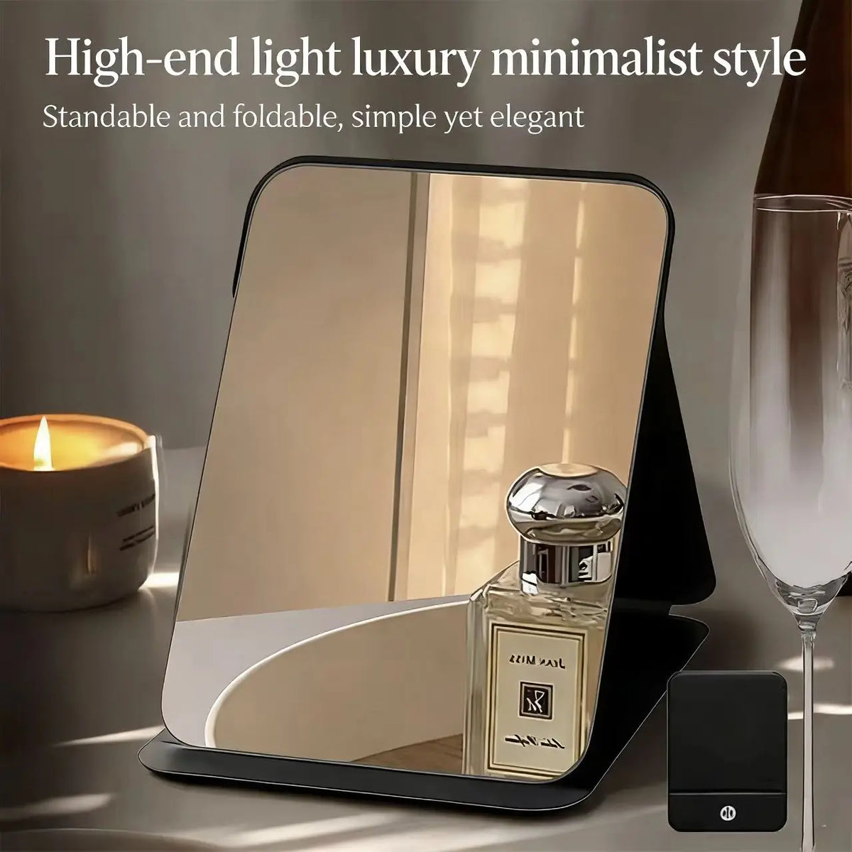 A high-end light luxury minimalist foldable makeup mirror resting on a dark surface next to a glass and a candle.