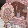 A pink hand holding makeup mirror set with decorative elements and a heart-shaped oval frame.