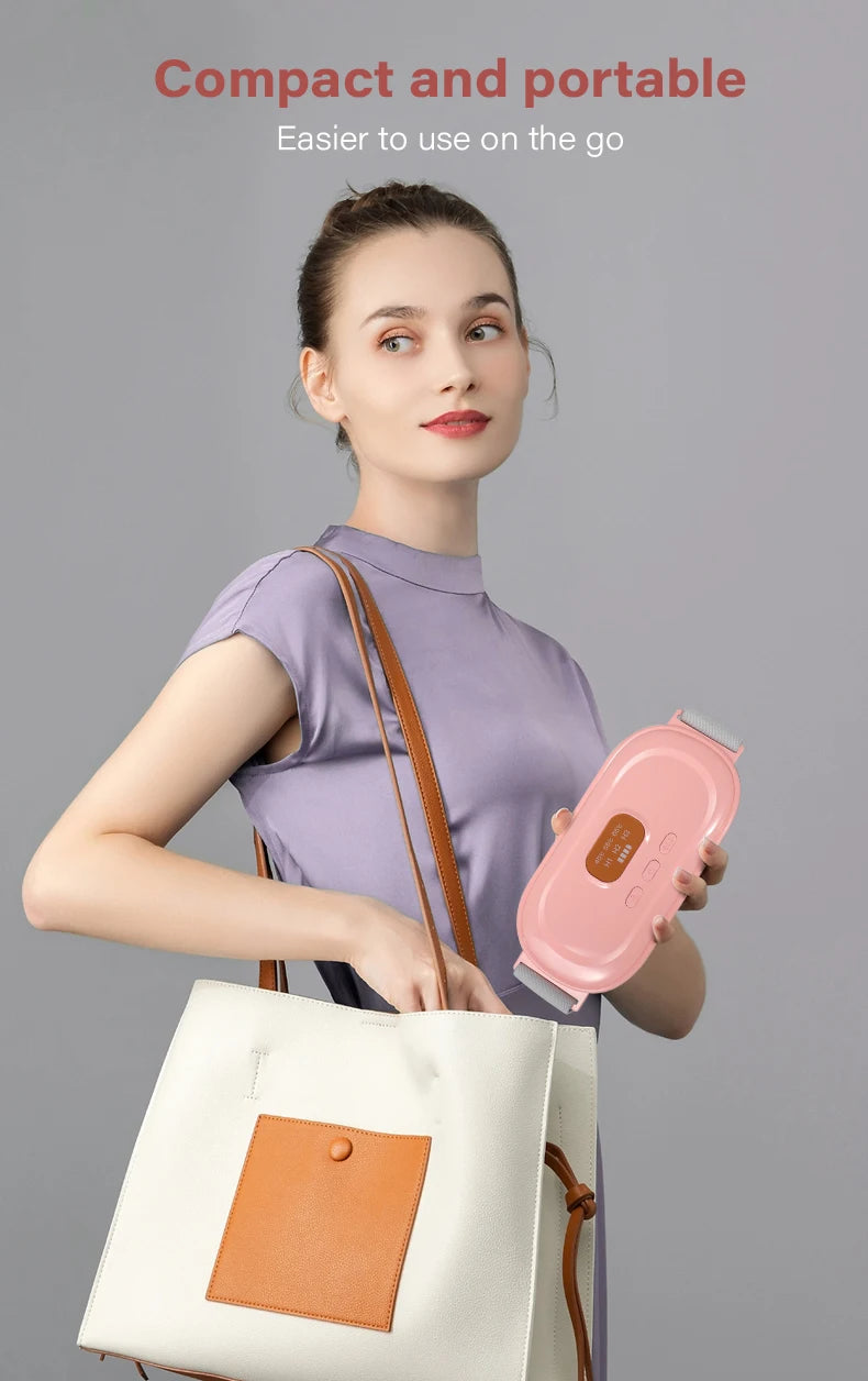 A woman holds a pink heated abdominal massage belt in her hand, against a gray background.