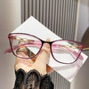 Une paire de lunettes à œil de chat roses avec détails en chaîne dorée, tenues sur un fond blanc.