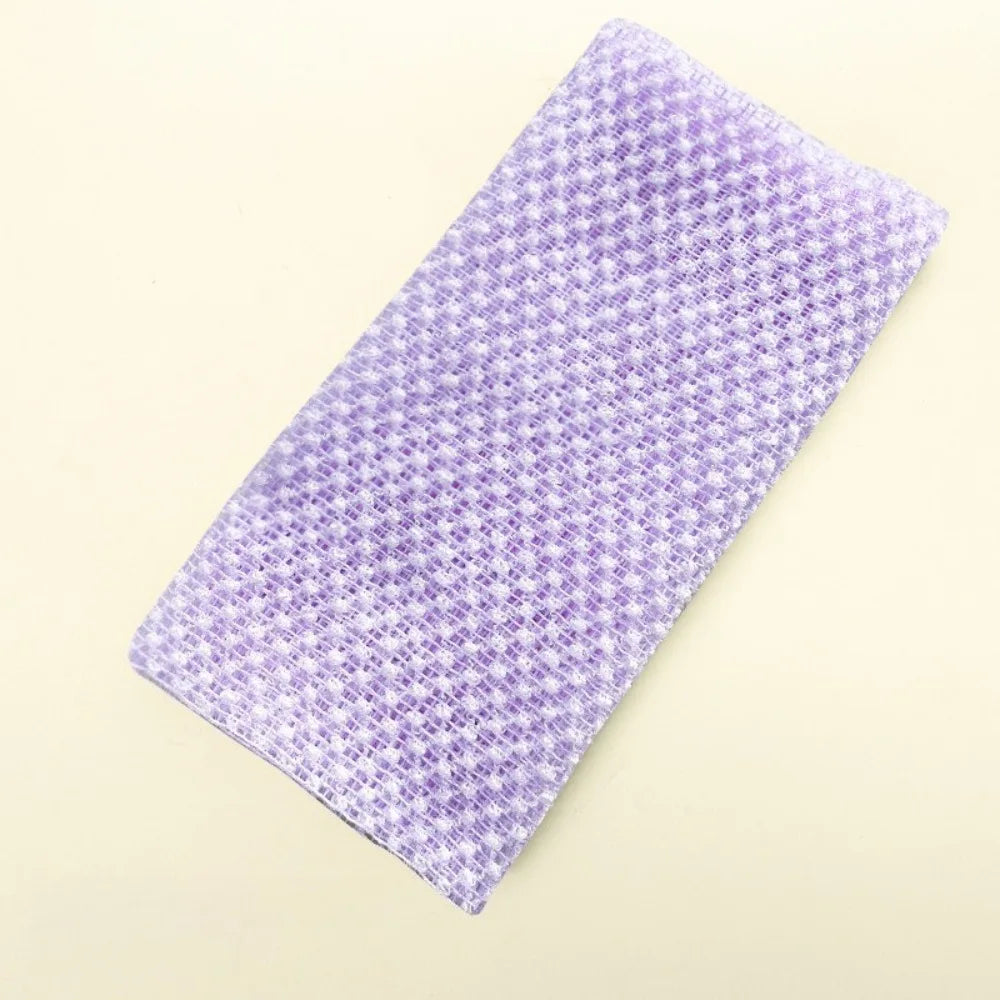 A purple exfoliating body scrubber loofah lying diagonally on a light background.