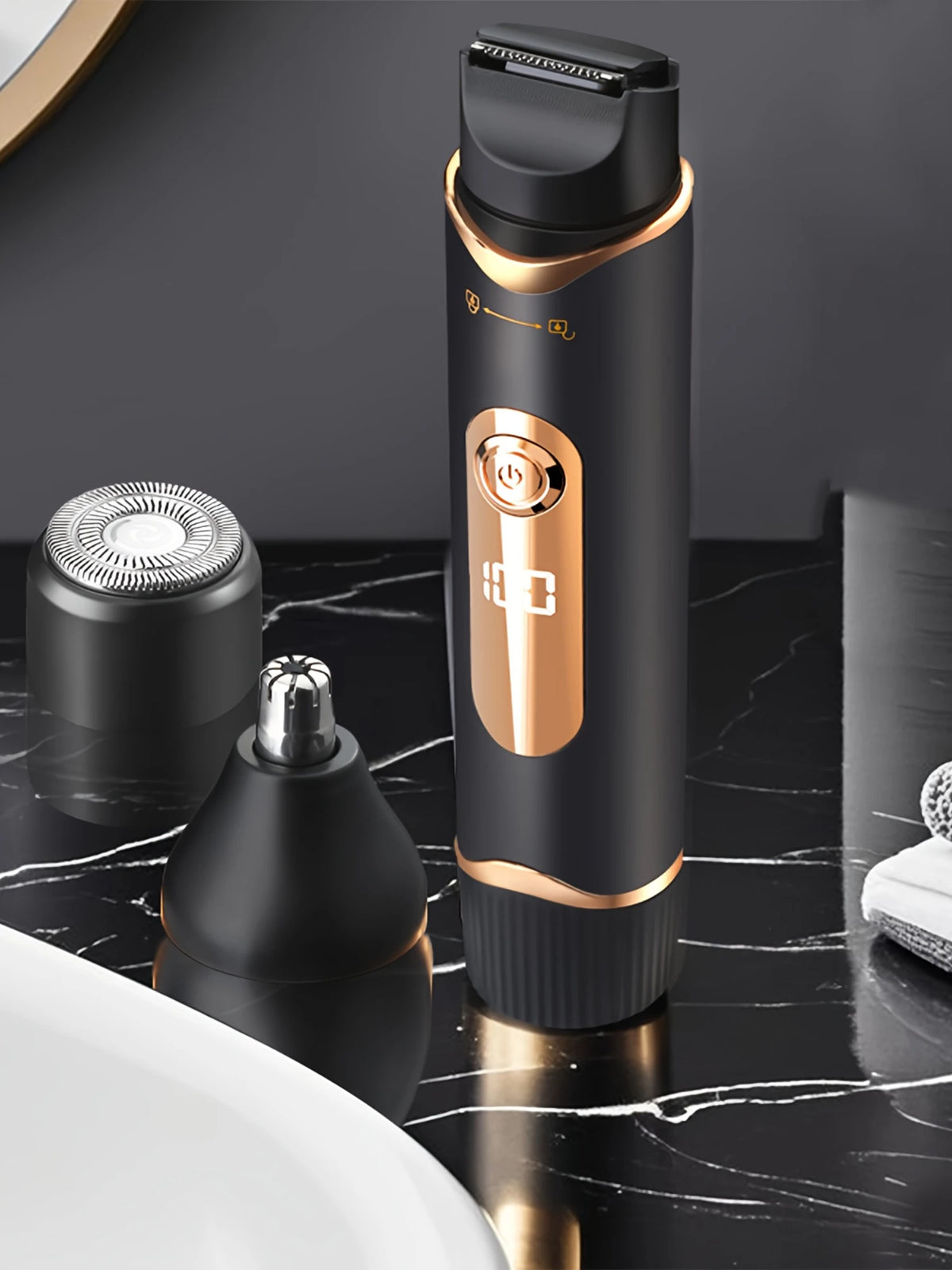A black electric body hair trimmer in a gold-accented casing is shown next to its detachable head on a dark marble surface.