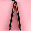 A black and gold professional ceramic flat iron hair straightener shown vertically against a pink background.