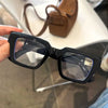 Une paire de lunettes à monture carrée rétro noires avec filtre de lumière bleue posée sur une surface blanche.