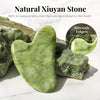 A smooth, light green jade stone is displayed on a white surface with other pieces of natural stone.