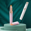 A pink and gold precision electric eyebrow trimmer is shown standing upright on a green surface.