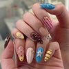 A hand displays a set of reusable pink and red striped press-on nails with various shapes on fingers.