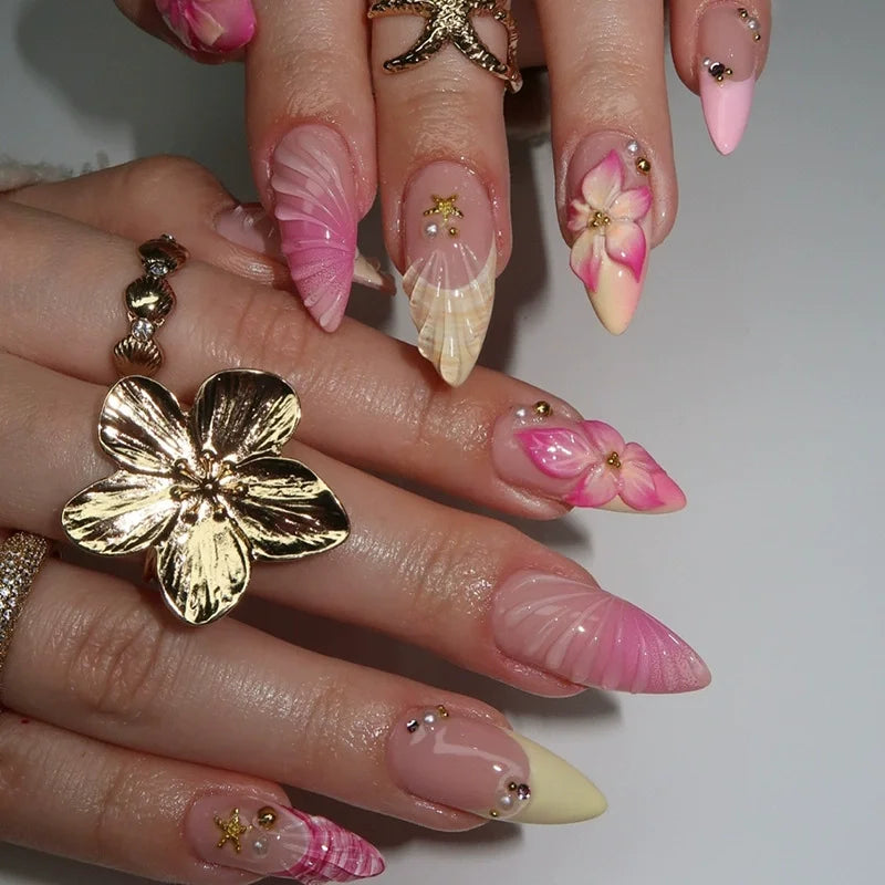 A hand displaying various press-on nails featuring floral and butterfly designs in pink, cream, and gold accents.