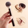 A hand holds a makeup brush and shows close-ups of the bristles and the brush tip.