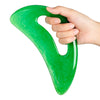 Una mano sostiene una herramienta gua sha de resina verde brillante con forma de corazón para masaje facial y corporal.