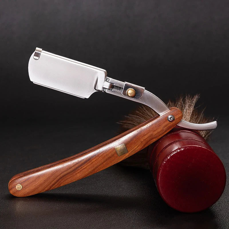 A silver shaving razor with a wooden handle and a leather grip resting on a dark surface.