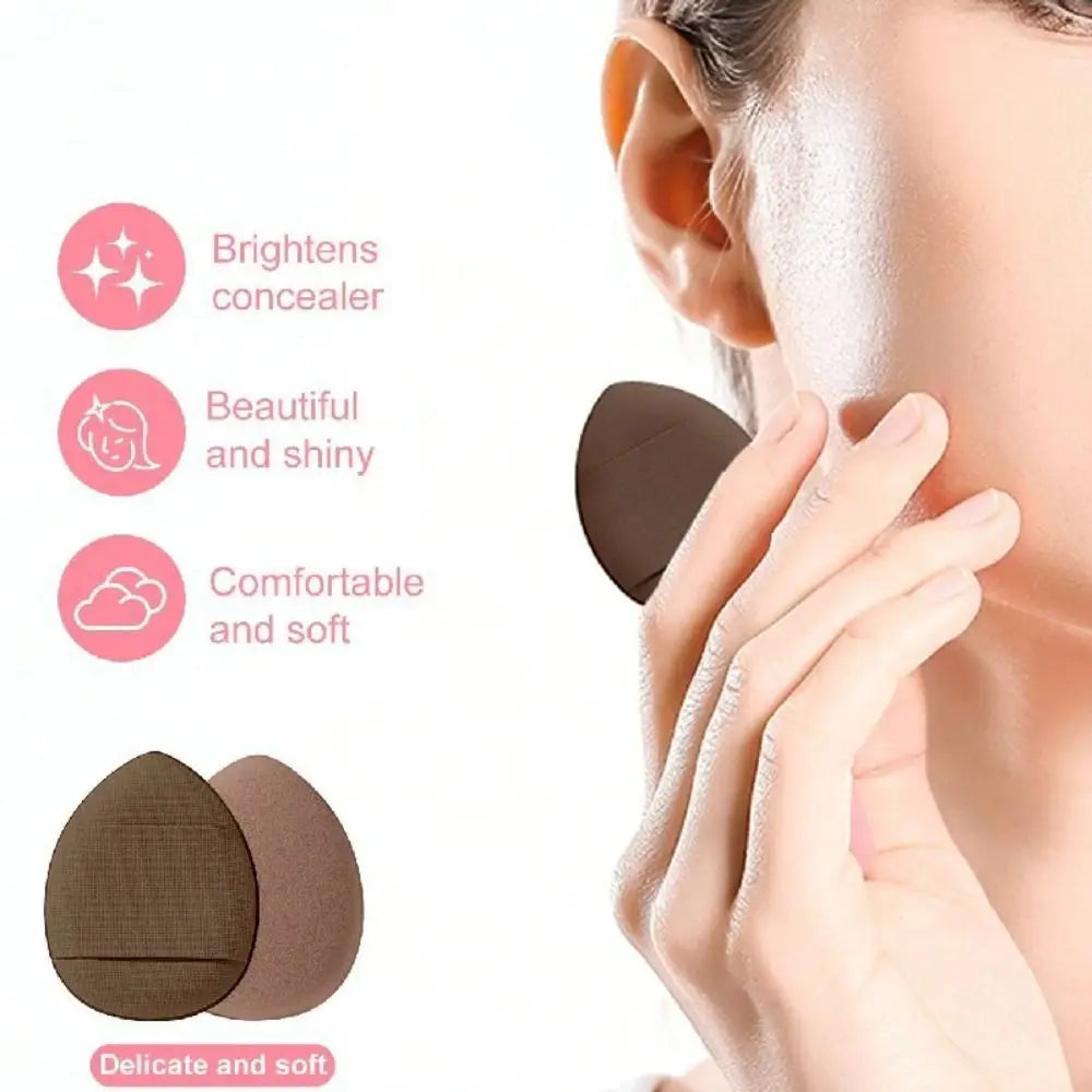 A hand is applying a makeup concealer using a soft, brown silicone tool on the skin.