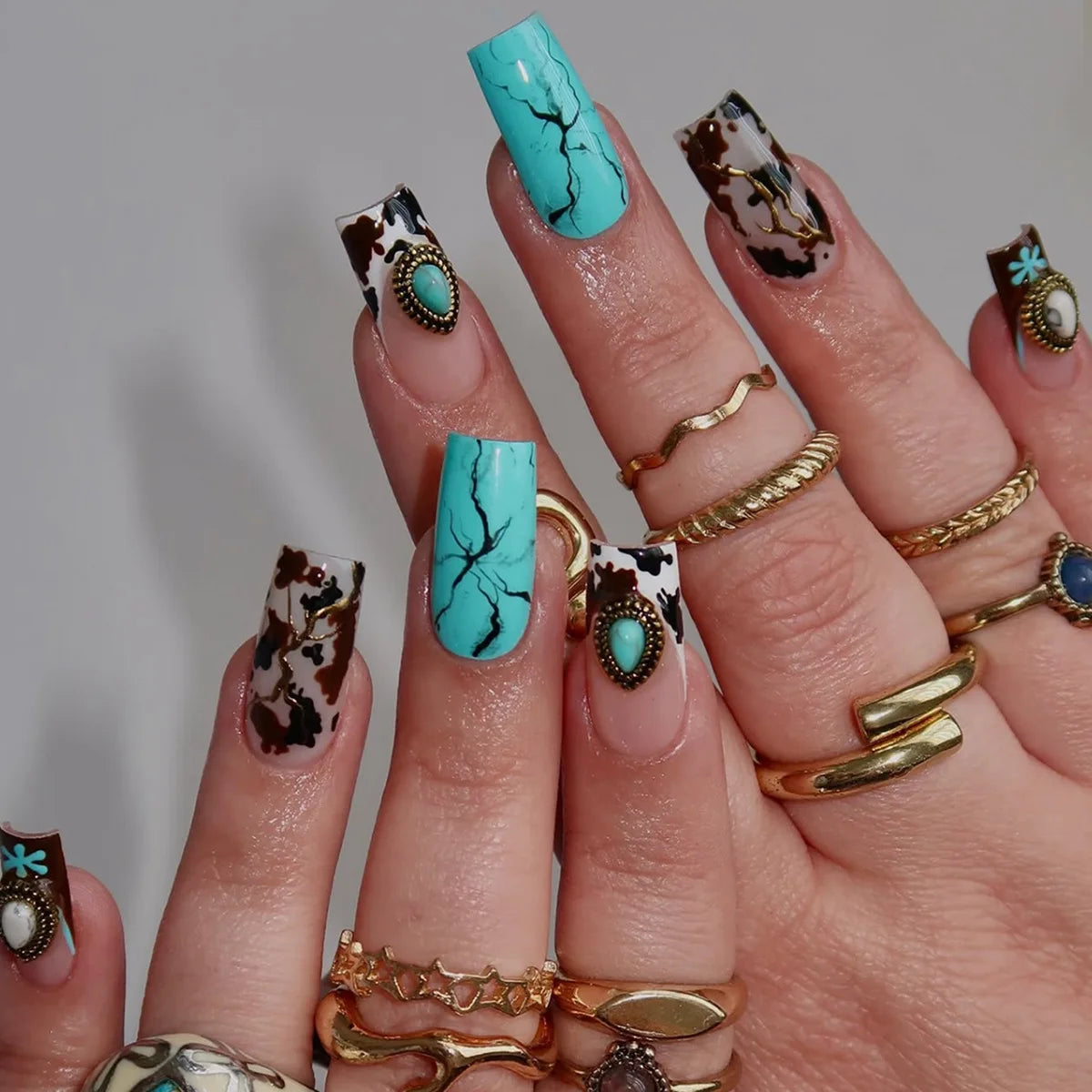 A hand displaying various Gothic Y2K press-on nails featuring marbled black and white designs with teal accents.